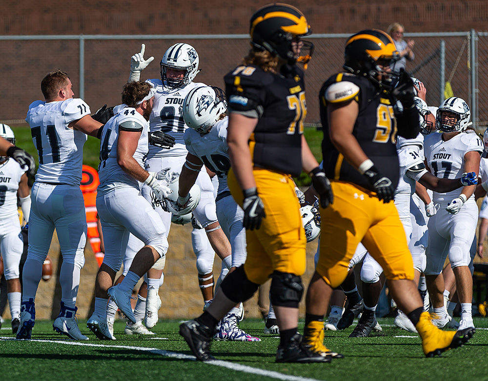 Scott Gustafson and teammates celebrate in the background, in focus, while Gustavus players walk off in the foreground