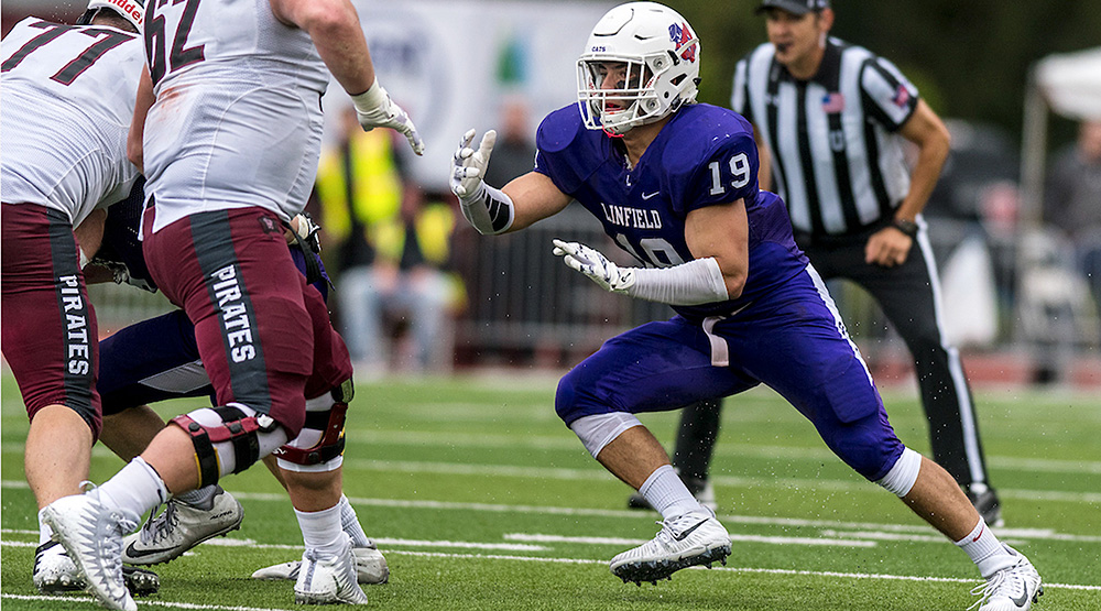Patrick Pipitone heads toward a pair of Whitworth offensive linemen (Linfield athletics photo)