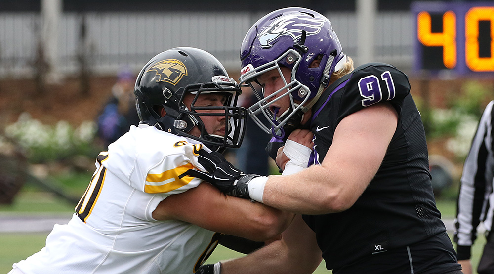 Oshkosh center Tyler Powers, in white jersey, squares off with UW-Whitewater defensive lineman Merritt Stott, in black jersey. (Photo by Daryl Tessmann, d3photography.com)